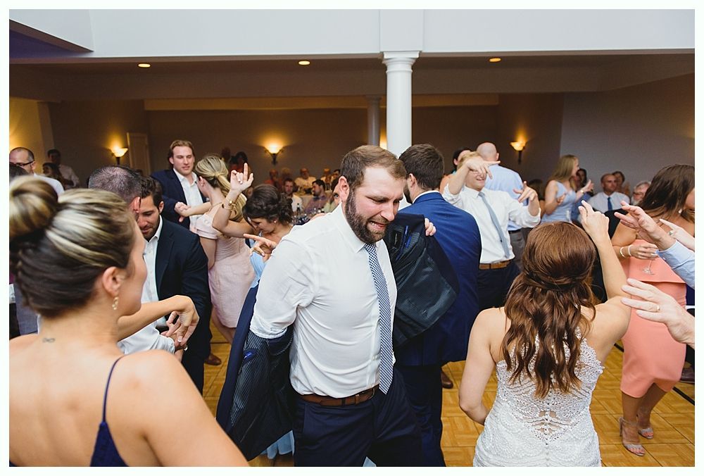 People dancing at a wedding reception; a man smiles with his jacket off, wooden floor.
