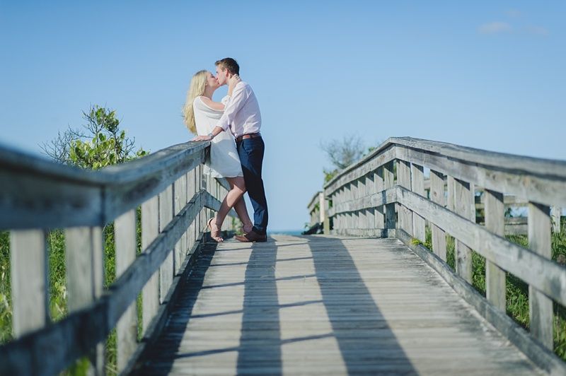 Couple in formal attire, smiling, close together, outdoors with autumn foliage.
