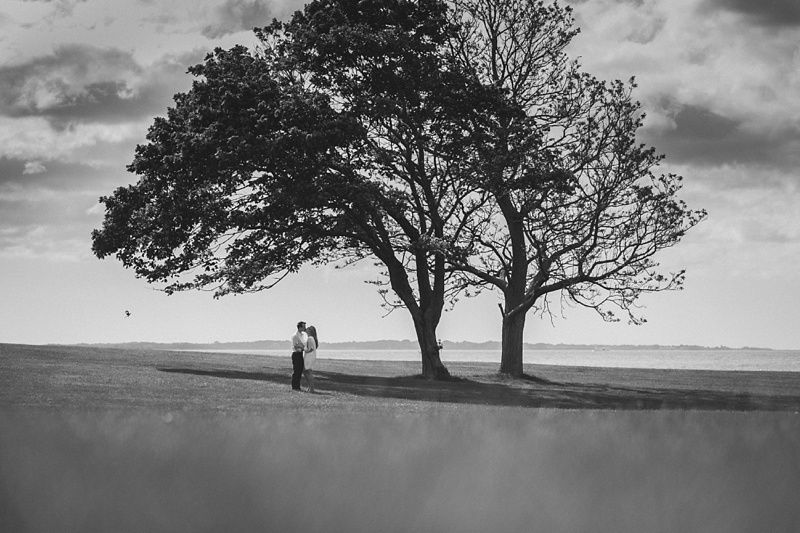 Couple in formal wear, woman in red and black outfit with gold embroidery, man in suit with red tie, smiling, intimate setting.