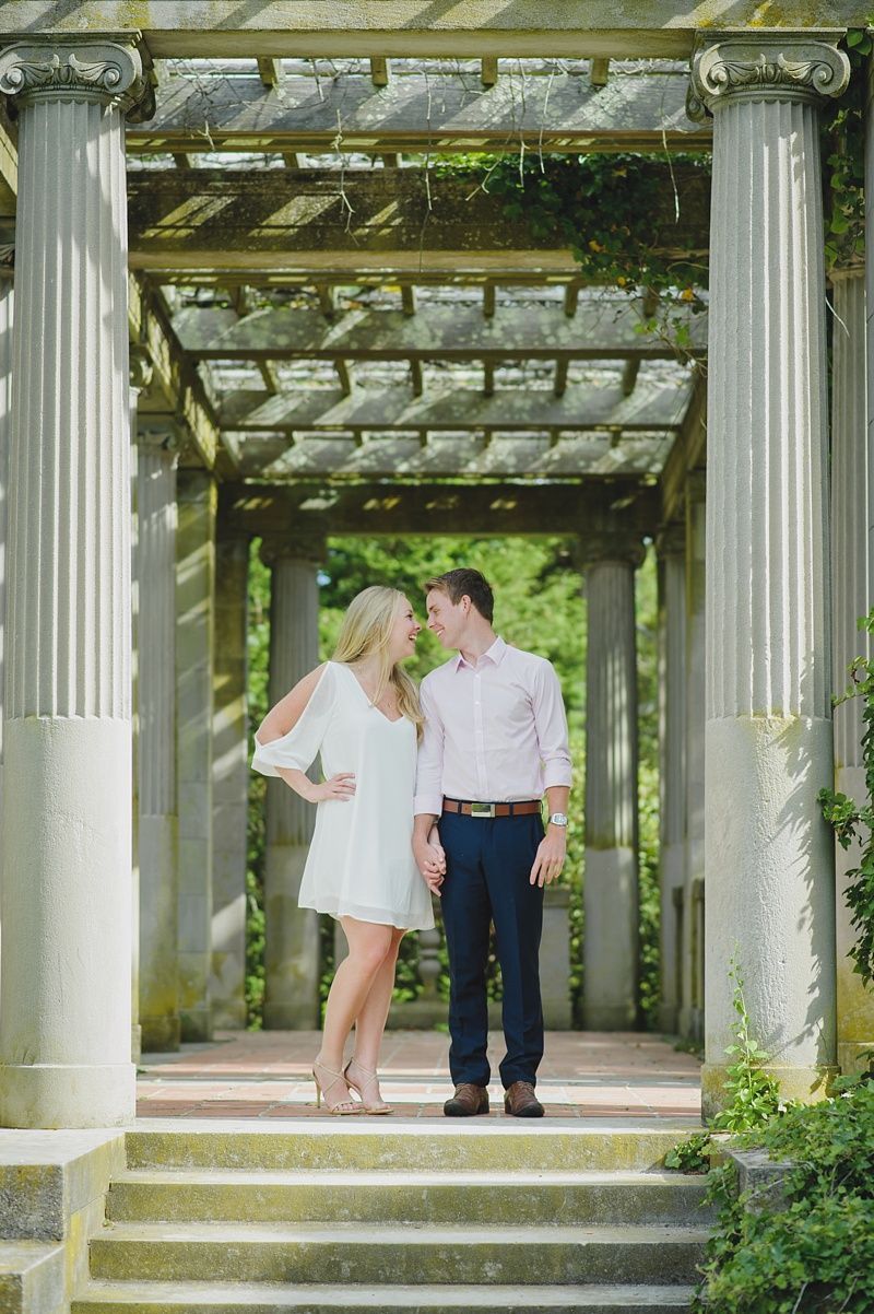 Couple in formal attire, posing outdoors in a park. Woman in red and gold traditional dress, man in a suit.