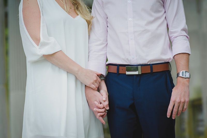 Couple holding hands walking on a grassy hill, under a tree with yellow-orange leaves, against a blue sky.