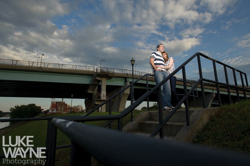 Couple embracing near a bridge. Cloudy sky overhead. Stairway in the foreground.