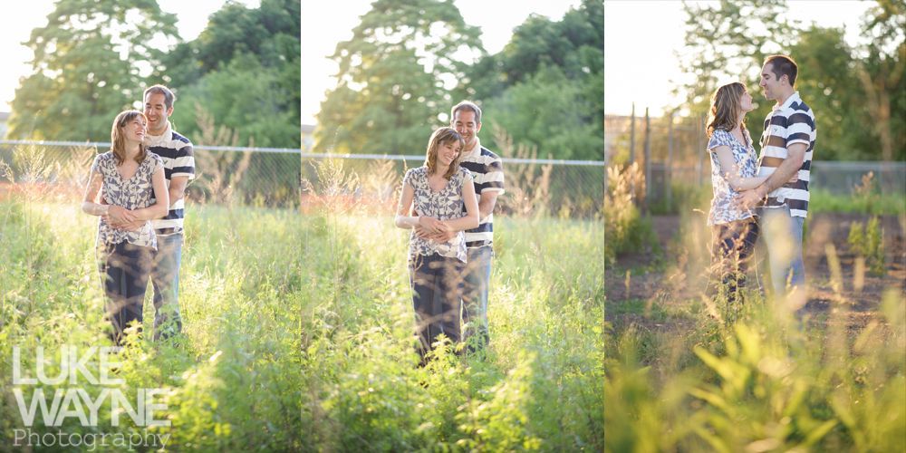 Couple embracing in a field of tall grass, sunlight shining, trees in background.