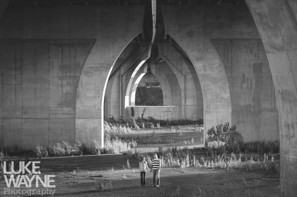 Two figures walk under large concrete arches, in a black and white photograph.