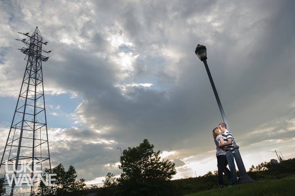 Couple kissing beside a lamppost, with power lines and cloudy sky in the background.