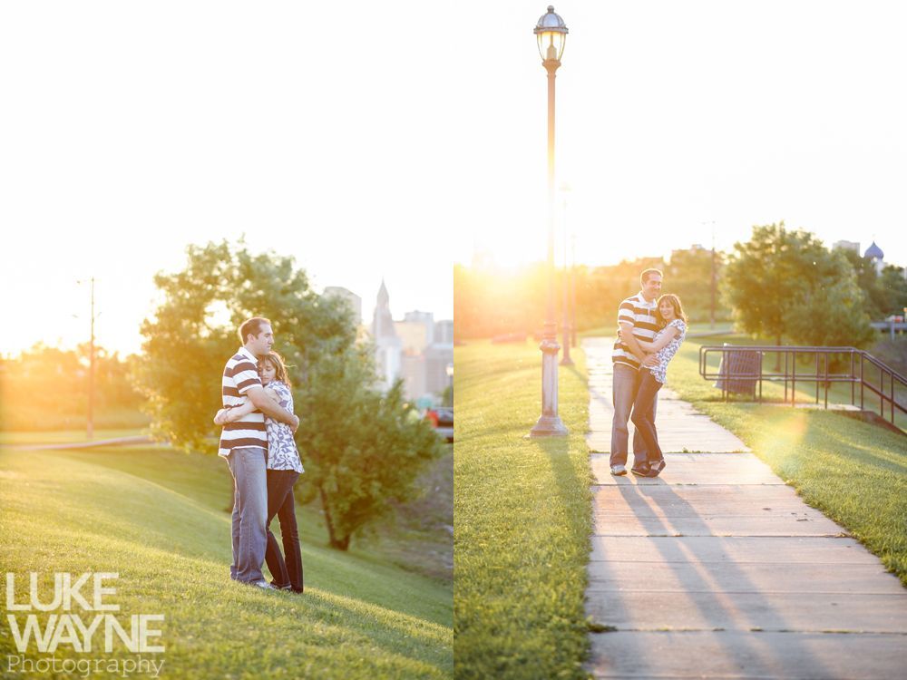 Couple hugging outdoors at sunset near a lamppost, casting long shadows on a grassy hill and walkway.