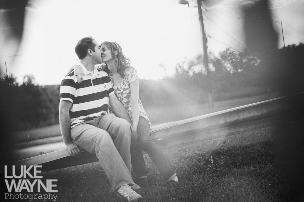 Couple kisses on a wooden fence, backlit by the sun. Black and white.