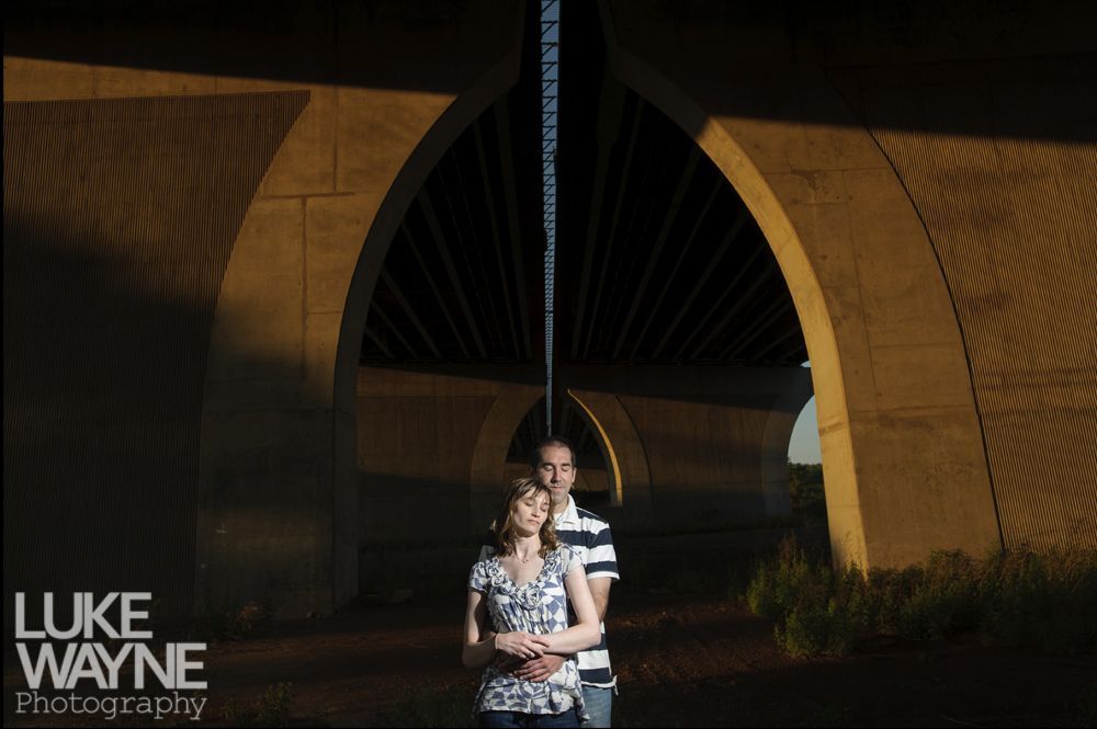 Couple embracing under arched bridge, warm sunlight illuminates the scene.
