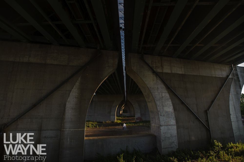 View from under a concrete bridge with arched supports, angled beams, and a glimpse of sky.