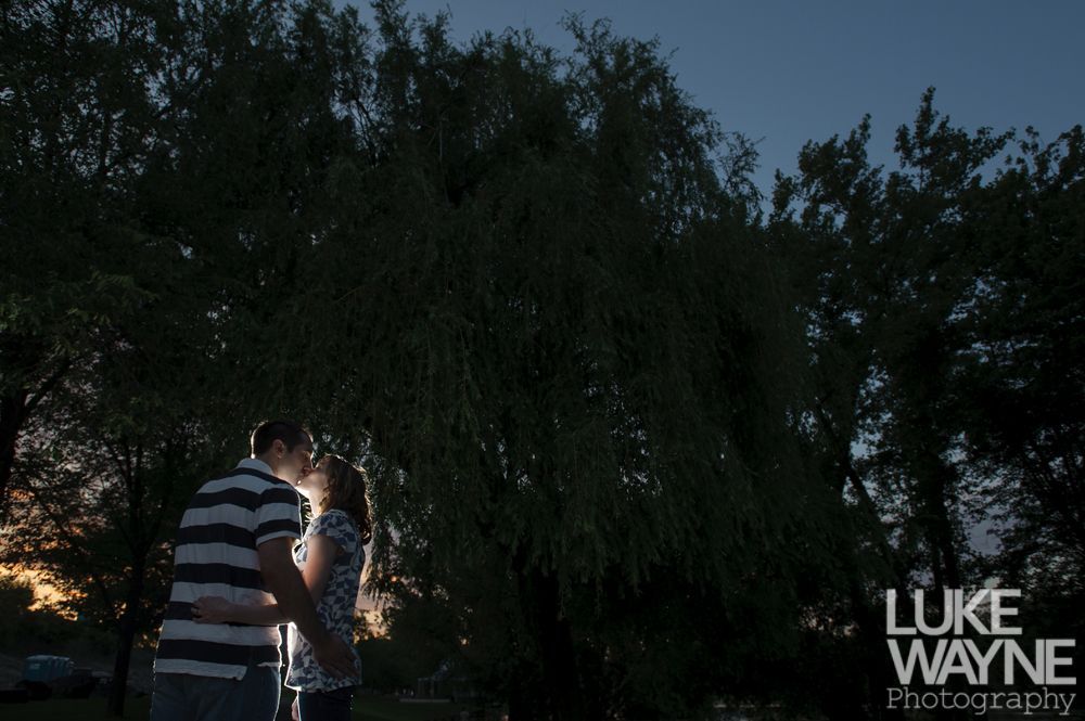 Couple kissing silhouetted by a tree at dusk.