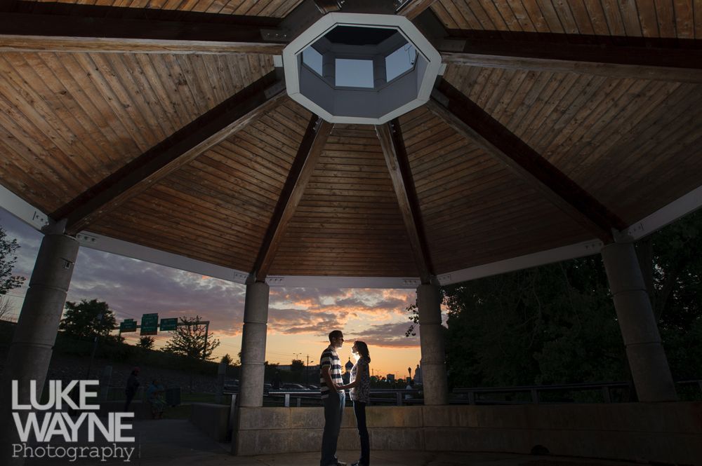 Couple silhouetted in gazebo, facing each other at sunset. Wooden ceiling, concrete pillars.