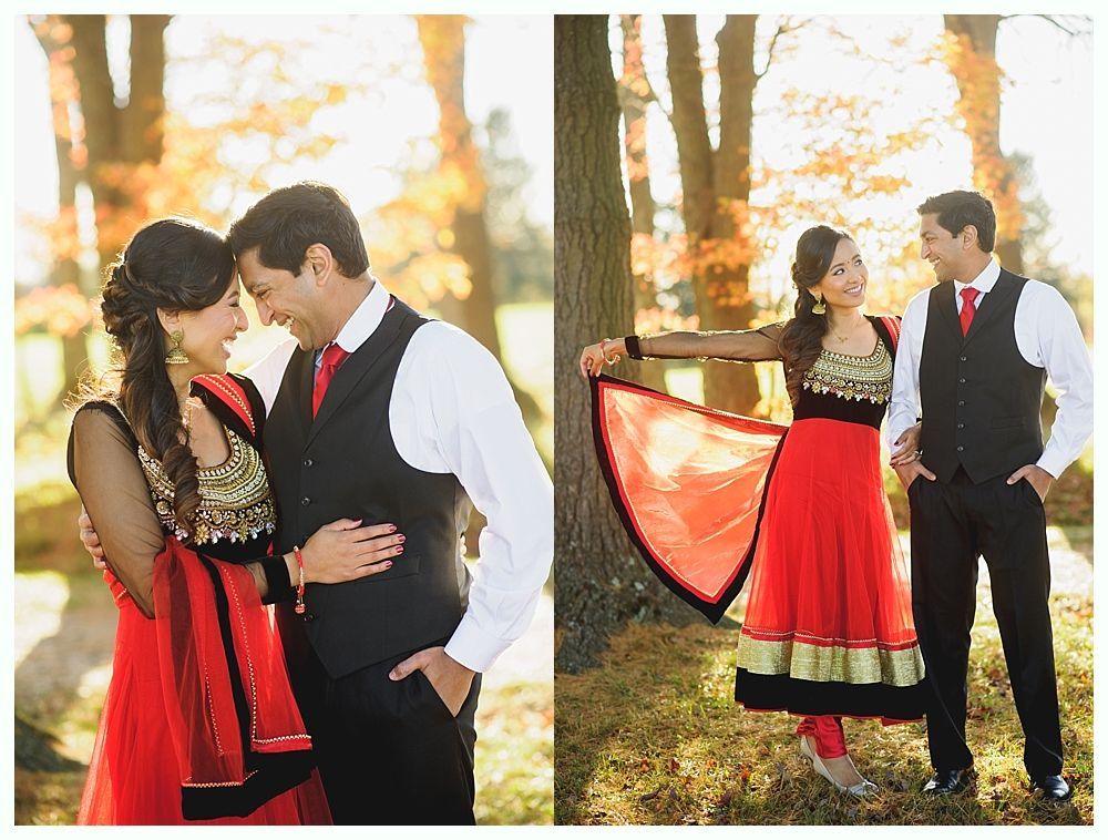Couple in formal wear, embracing and smiling in a park with autumn foliage. The woman wears a red and gold dress, and the man a vest and tie.