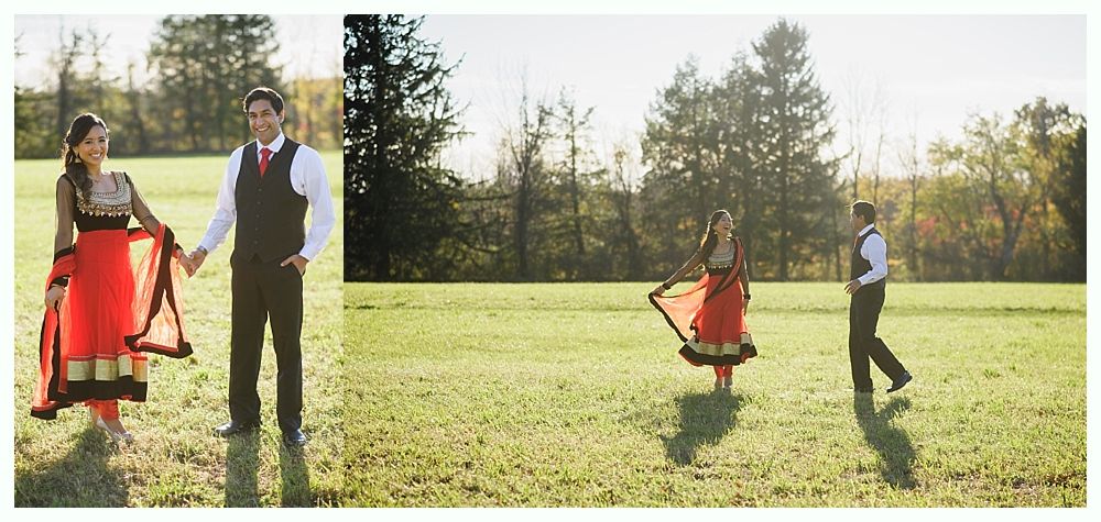 Couple holding hands in a field, woman twirling. They wear formal clothing, trees in the background, sunny day.