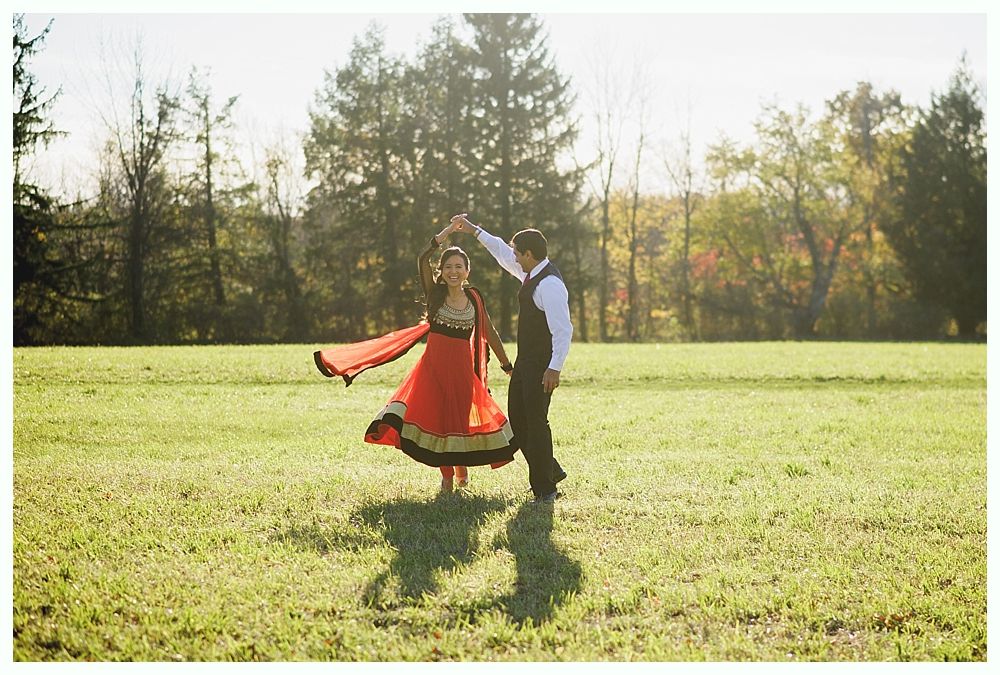 Couple dancing in a sunlit field, woman in red and gold dress, man in vest.