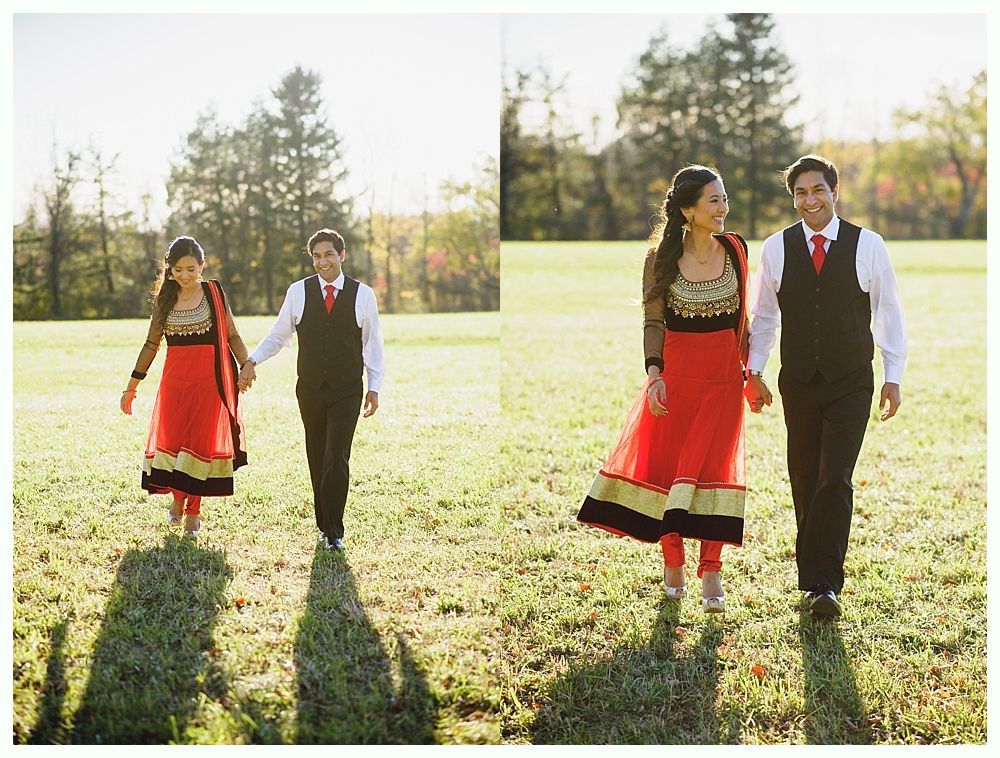 Couple walking and holding hands in a field; the woman in a red and gold dress, the man in a black vest.