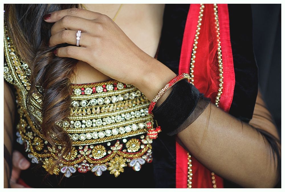 Woman's hand with ring on ornate clothing, with black sleeves, red accents and curly hair.