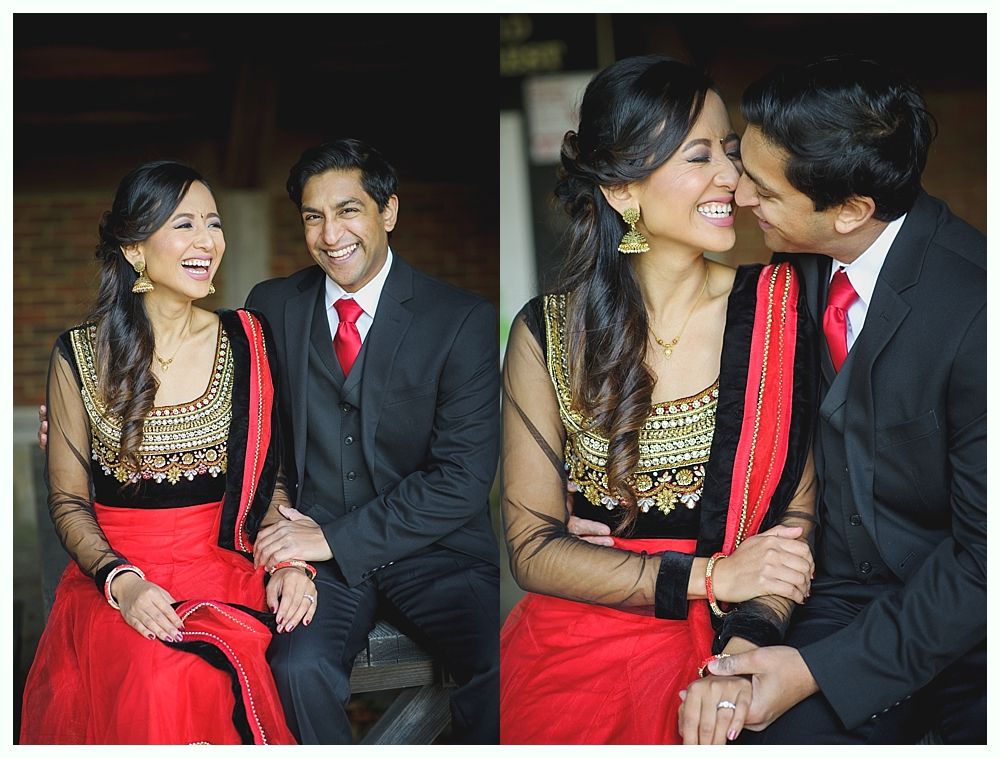Couple in formal wear laughing, outdoors. Woman in red sari with gold accents. Man in black suit with red tie.