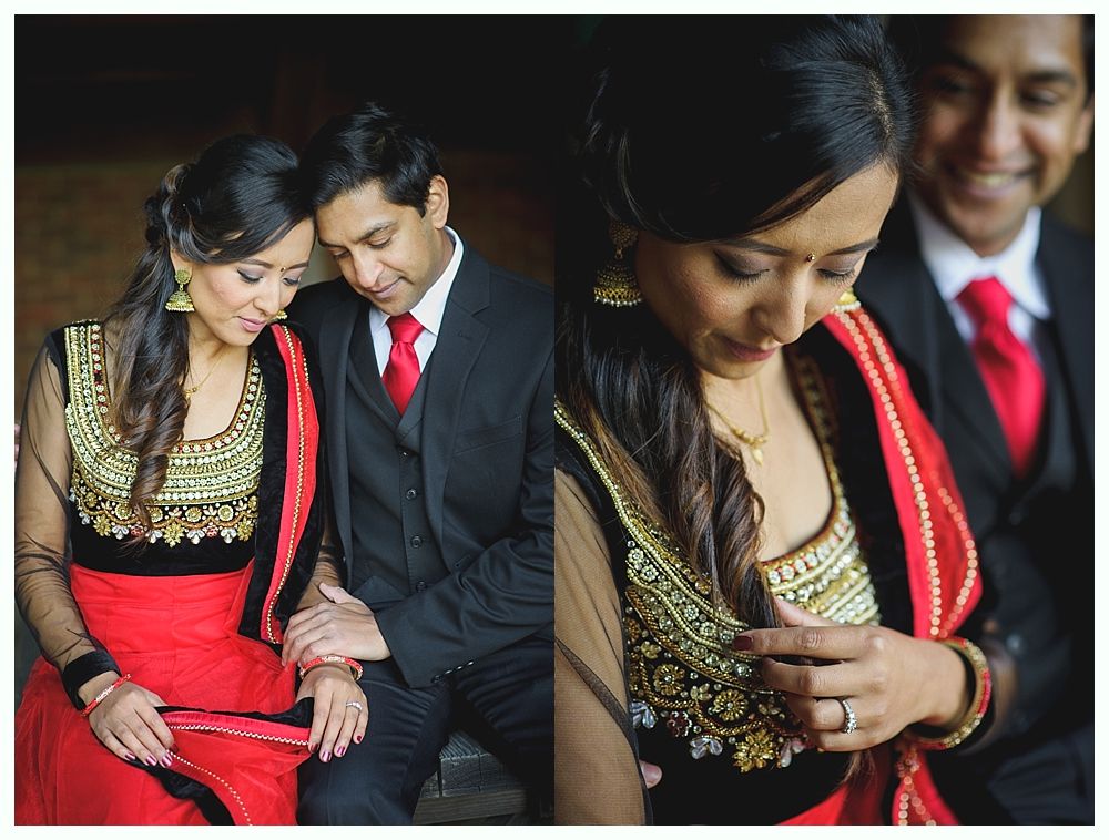 Couple in formal wear, woman in red and black outfit with gold embroidery, man in suit with red tie, smiling, intimate setting.