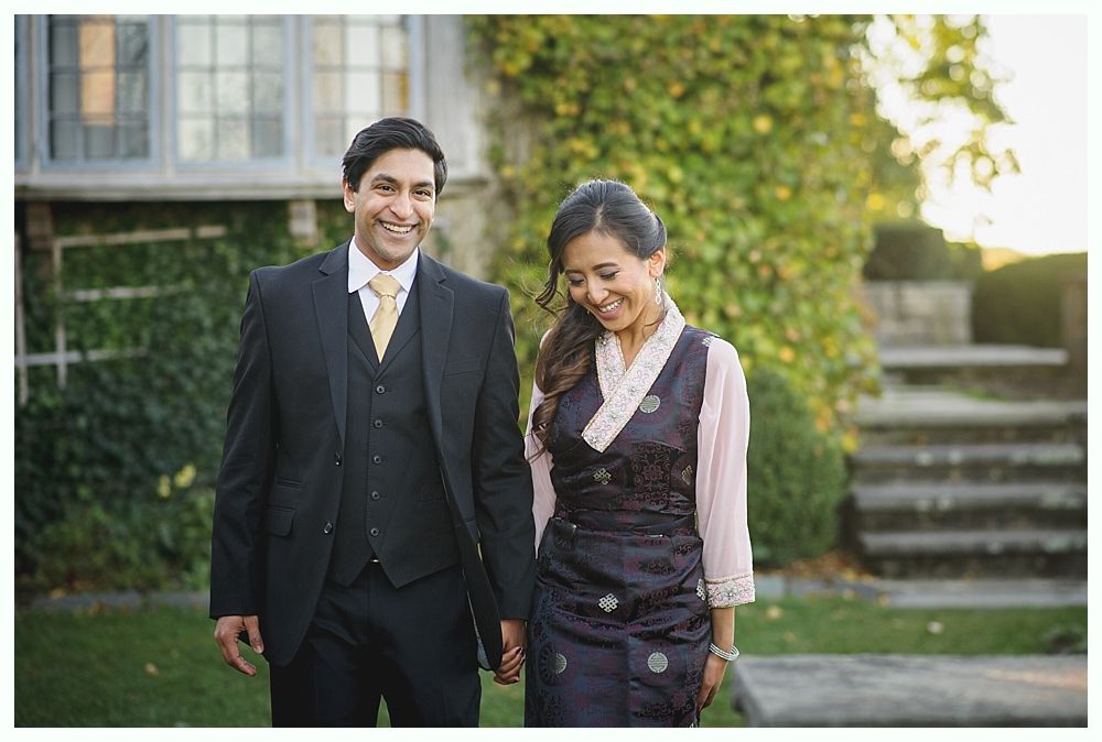 Couple holding hands, smiling, walking outdoors; man in suit, woman in traditional dress.
