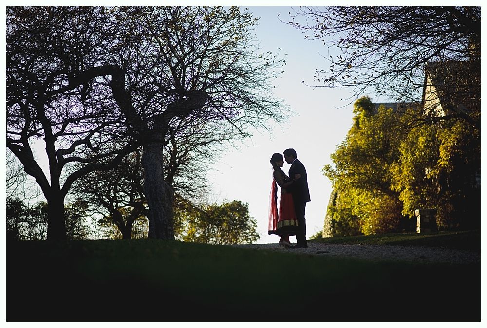 Couple silhouetted embracing on a path, trees framing them, golden light.