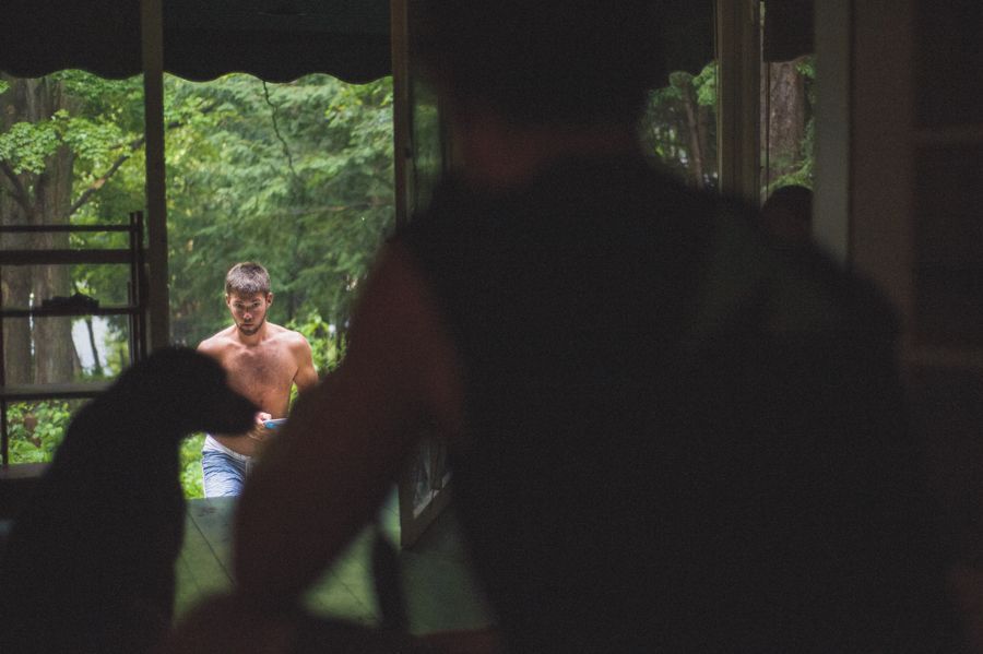 Bride walks down a path with two men, holding a yellow bouquet. Fountain and building in the background.
