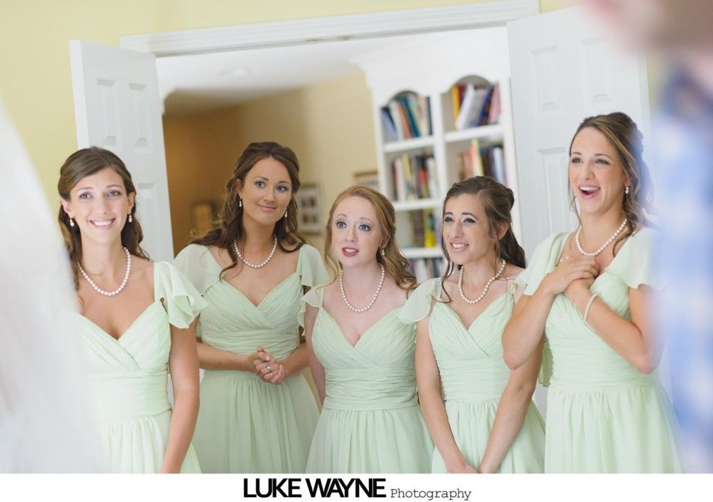Five women in mint green dresses react with surprise, standing by an open doorway.