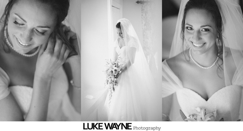 Bride in wedding dress, adjusting earring, holding bouquet, smiling. Black and white.