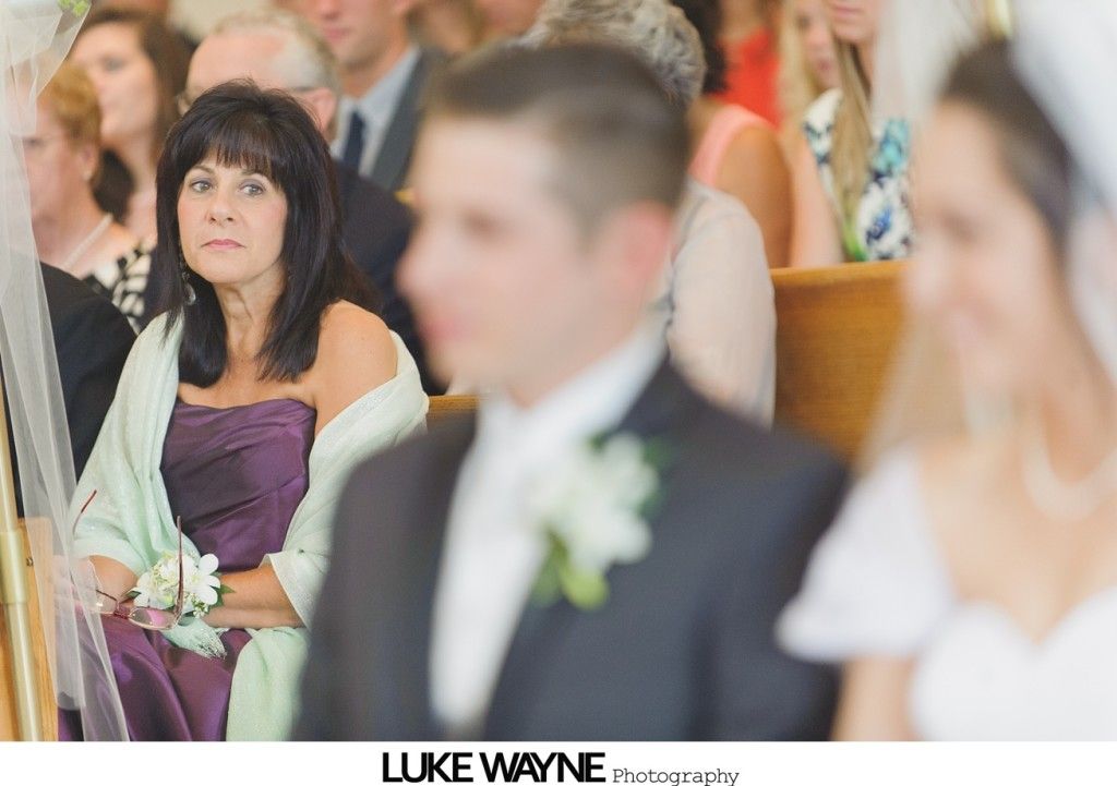 Woman in purple dress and shawl watches a wedding ceremony; groom and bride in foreground.