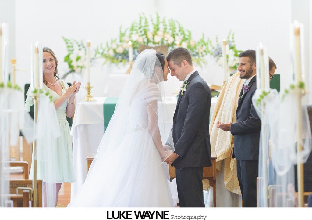 Bride and groom touch foreheads, holding hands, during a church wedding ceremony.