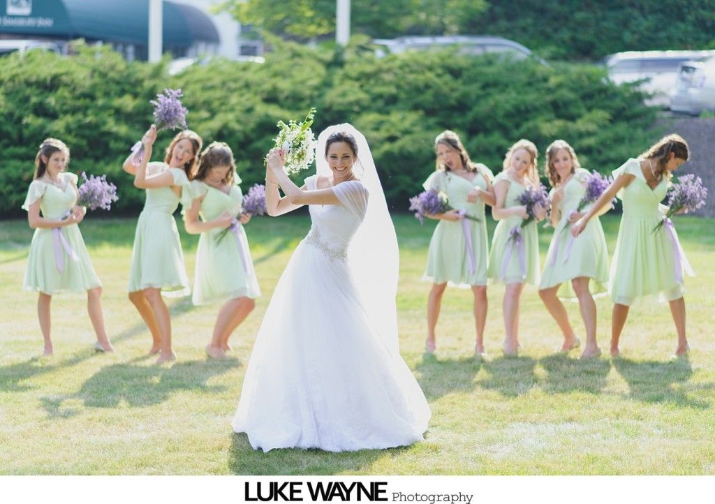 Bride dancing with bridesmaids in matching green dresses, holding bouquets outdoors.