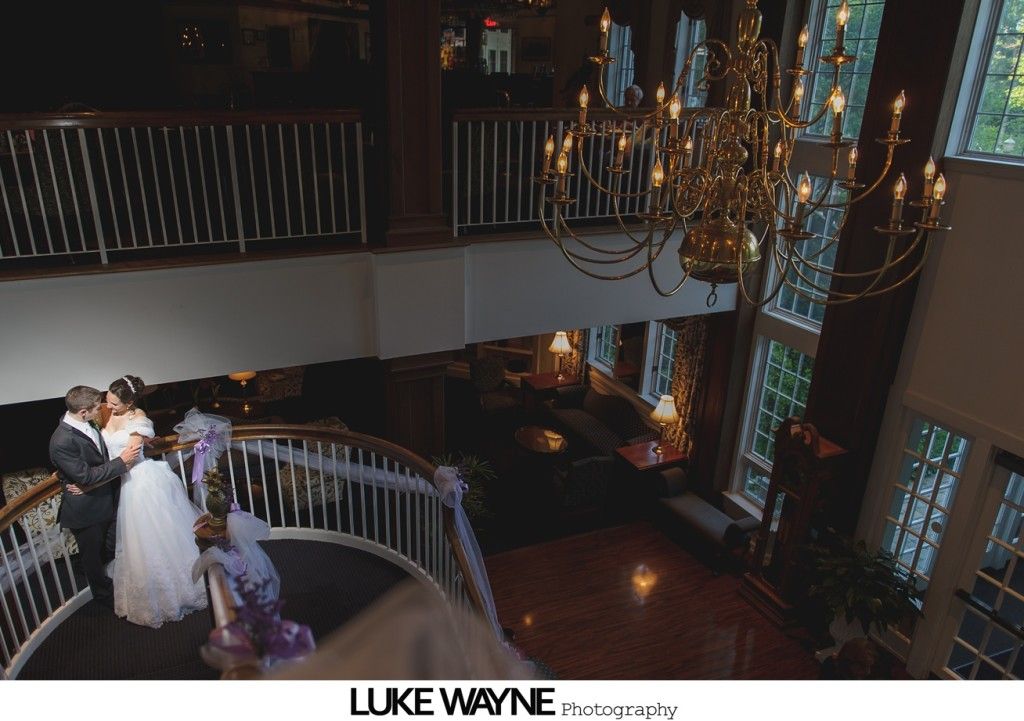 Wedding party on curved staircase beneath a chandelier, elegant indoor setting.