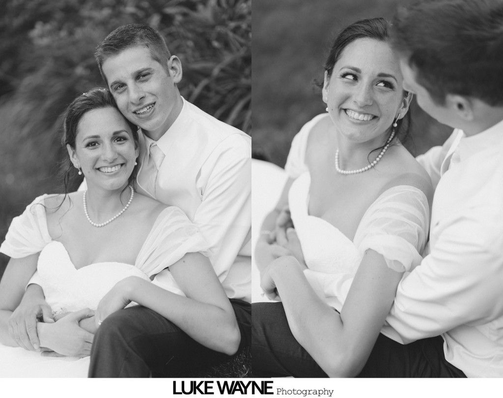 Bride and groom embrace outdoors; bride smiles at groom. Black and white.