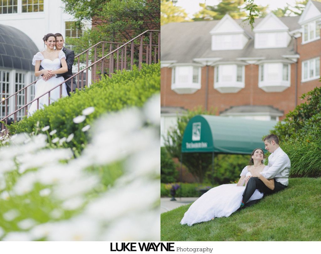Bride and groom pose on a hillside with flowers and a building in the background.