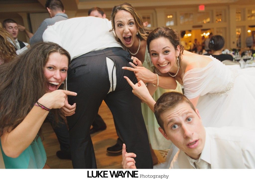 People playfully touching a person's pants, several smiling at a wedding reception.