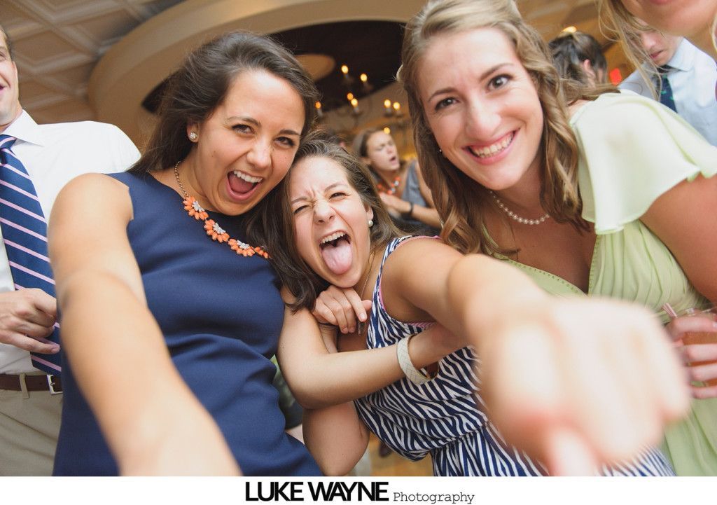 Three women smiling, yelling, and pointing towards the camera, at a party or event.