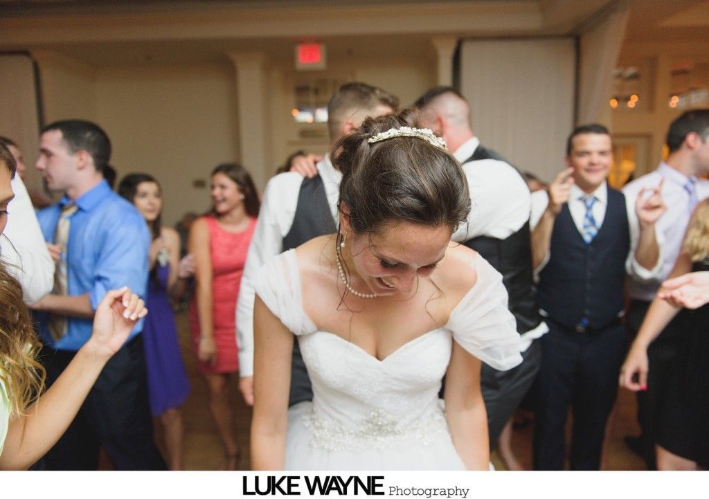 Bride dances at a reception, wearing white dress with veil, surrounded by guests.