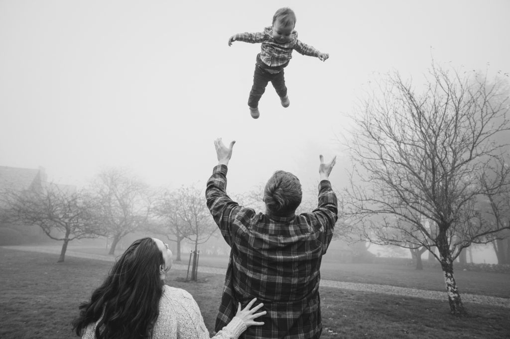 A child in mid-air above parents with outstretched arms on a foggy day.