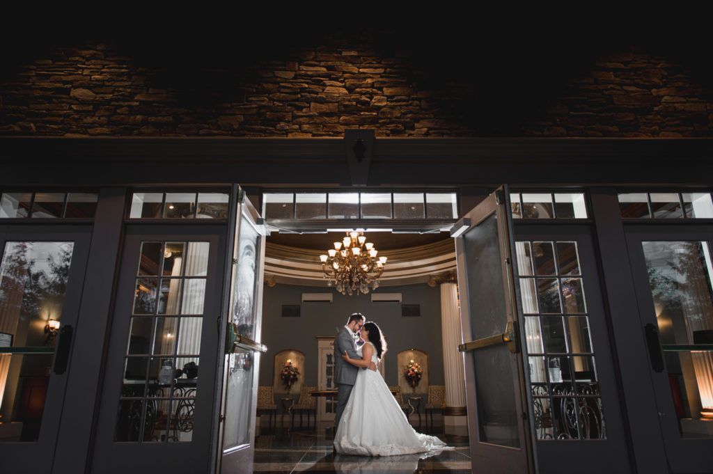 Couple embracing, kissing in doorway. Wedding photo with chandelier in background.