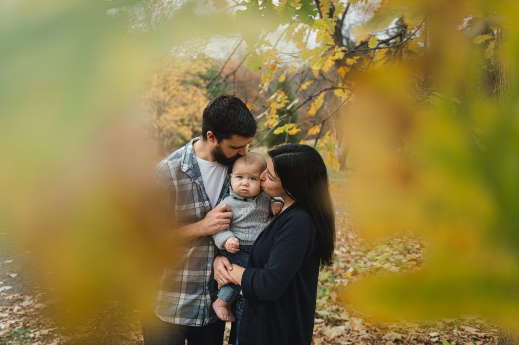 Woman holding a baby outdoors, both looking at each other, surrounded by fall foliage.