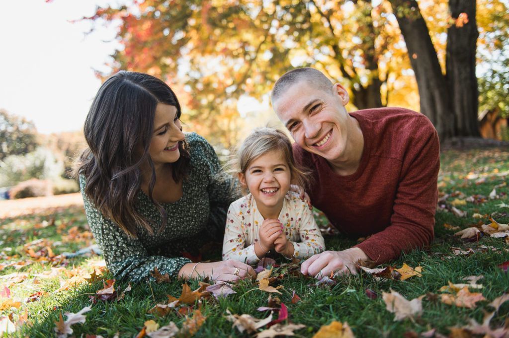 Family laying on grass, smiling, autumn leaves.
