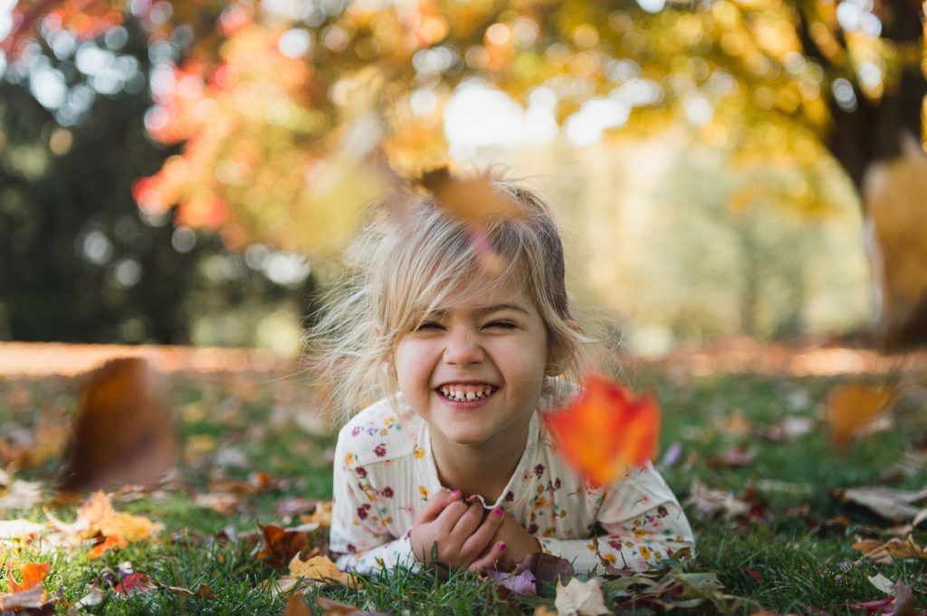 Family laying on grass, smiling, autumn leaves.