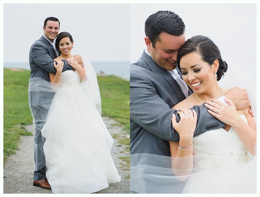 Bride and groom embrace outdoors, she in a white gown, he in a gray suit; both smiling.
