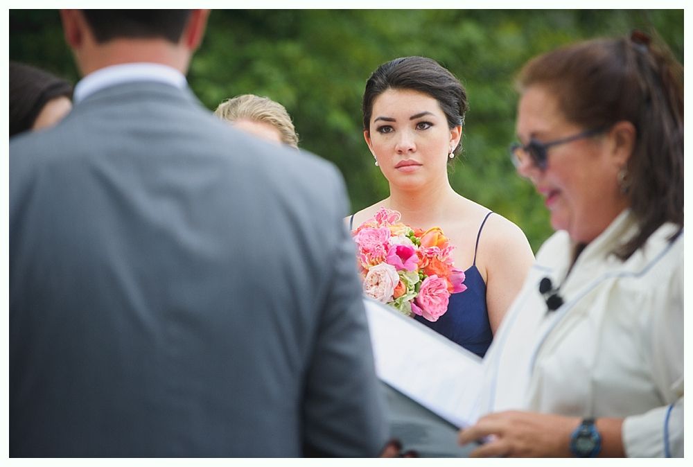 Woman in a blue dress holding flowers, looking intently during a ceremony. Others are in attendance.