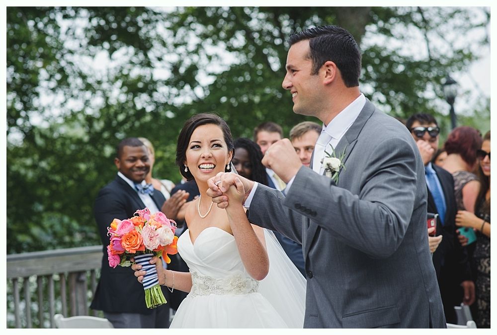 Bride and groom celebrating after wedding ceremony; bride holding bouquet, both smiling, surrounded by guests.