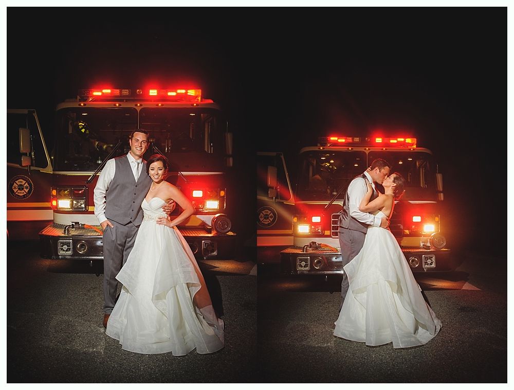 Newlyweds pose in front of a fire truck at night with flashing red lights.