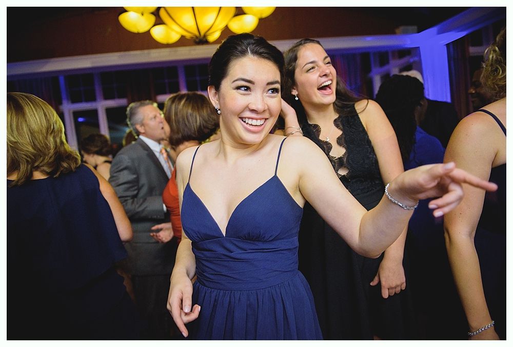Woman in blue dress smiles and points, dancing with friends at an event.