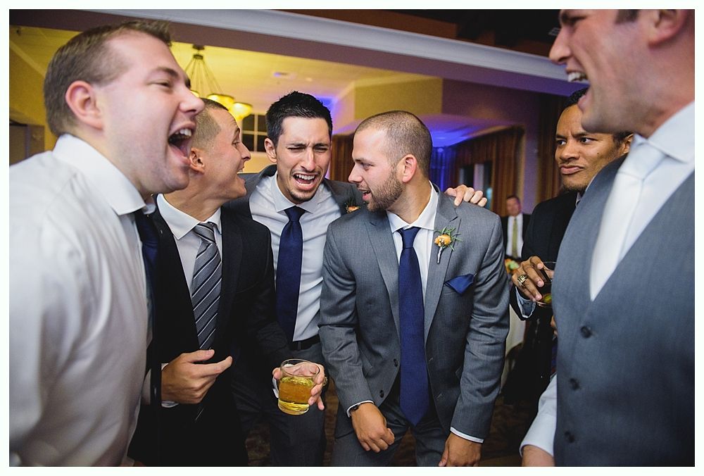 Men in suits laughing together at a party, one holding a drink.