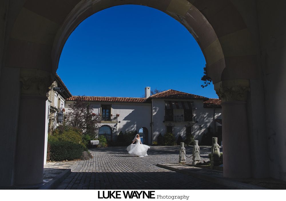 Bride smiles surrounded by teal-clad bridesmaids, holding bouquets in an orchard.