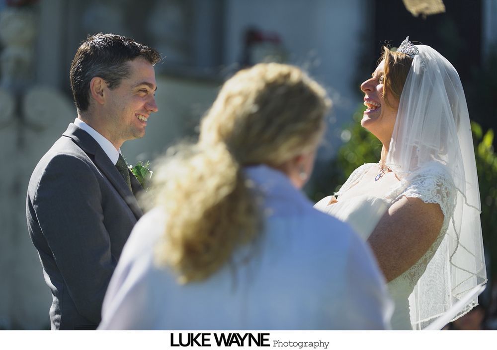 Couple kissing under a large, autumn-colored tree on a sunny, grassy hill.