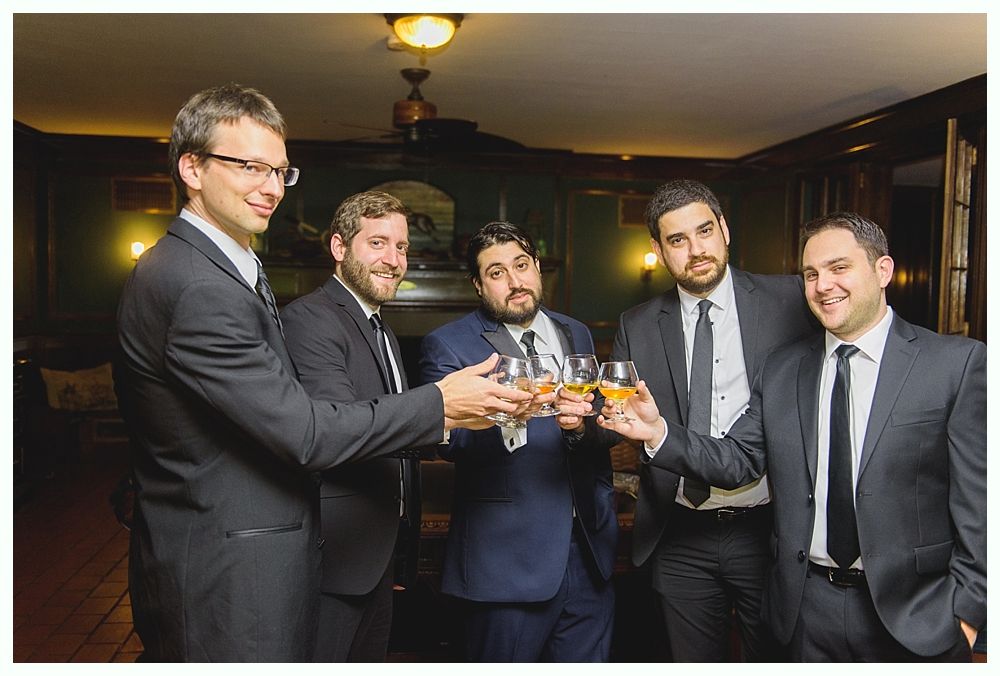Five men in suits toasting with glasses of amber liquid in a dimly lit room.
